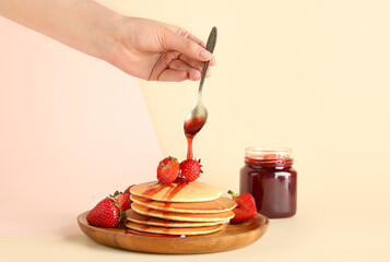 Woman adding sweet strawberry jam onto pancakes on beige background