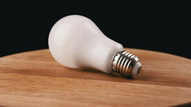 One Energy Saving Light Bulbs Spinning on a Wooden Board, Black Background. Round white LED bulb. Side view. Blurred motion. Selective focus. Rotation by circle. Copy space. Place for text. Isolated.
