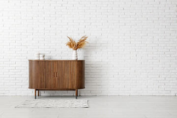 Modern chest of drawers with pampas grass and decor near light brick wall in room