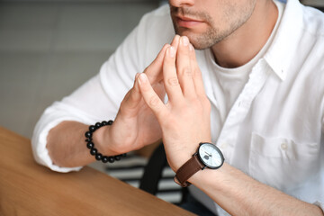 Stylish young man with wristwatch sitting in office, closeup