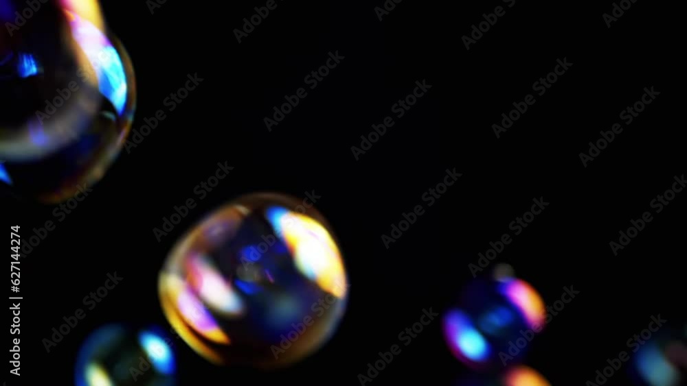 Poster colorful soap bubbles fly in an empty space on isolated black background. many large, small rainbow 