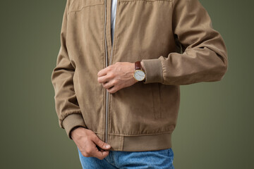 Stylish young handsome man with wristwatch zipping jacket on olive background