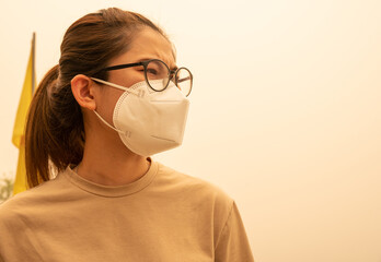 Worried Asian woman wearing an N95 mask for protect bad air pollution. PM2.5 levels meaning the air...