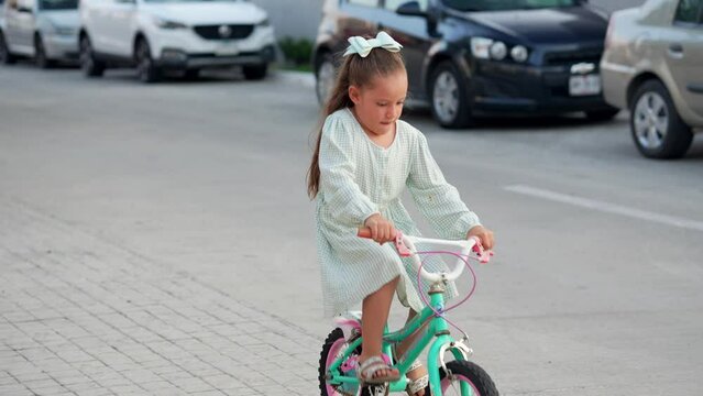 Ni&ntilde;a feliz rubia latina mexicana sonriente aprende a montar en bicicleta por las calles de su vecindario en vacaciones en un caluroso verano al atardecer al aire libre soleado