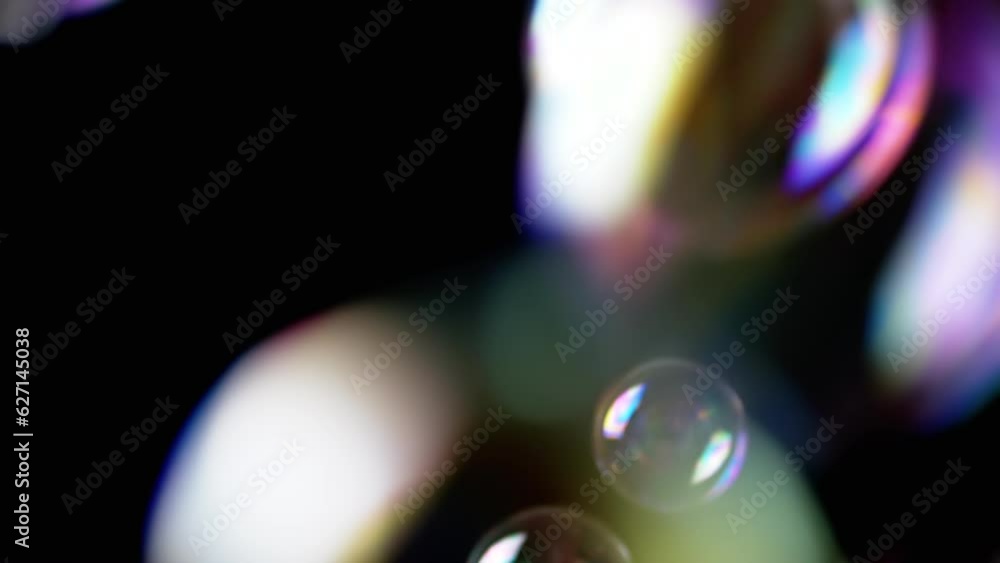Poster colorful soap bubbles fly in an empty space on isolated black background. many large, small rainbow 