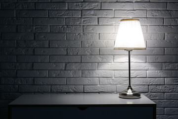 Glowing lamp on table near white brick wall in dark room