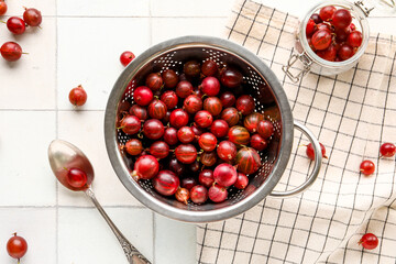 Colander and jar with fresh gooseberries on white tile background