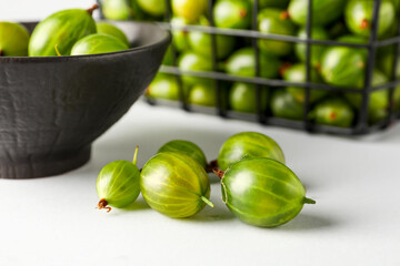 Bowl and basket with fresh gooseberries on white background