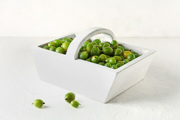Basket with fresh gooseberries on white background
