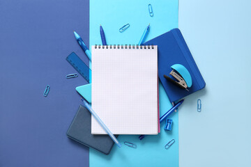 Composition with blank notebook and different school stationery on blue background