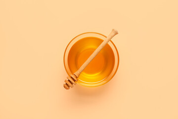 Glass bowl of sweet honey and dipper on beige background