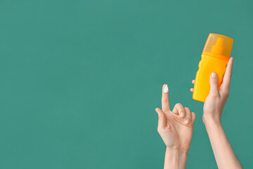 Female hand with bottle of sunscreen cream on green background