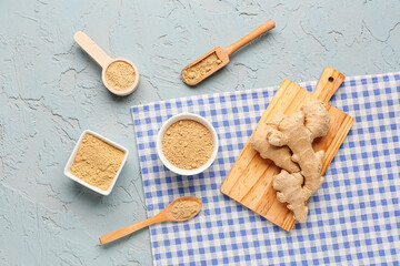 Fresh ginger root, bowls and wooden spoons with dried powder on blue background