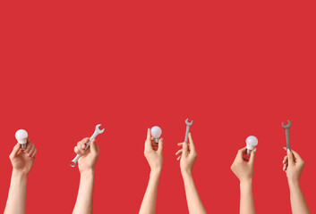 Electrician hands with light bulbs and wrenches on red background