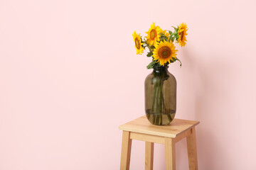 Vase with beautiful sunflowers on stool near pink wall in room