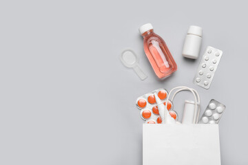 Paper bag with different pills and bottles of medicines on grey background