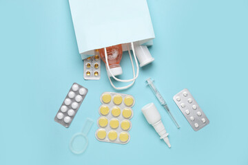 Paper bag with different pills, syringe and bottles of medicines on blue background