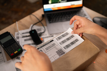 Woman employee glue barcode on delivery parcel. Worker packing cardboard packages before delivery at storage. Women working in factory warehouse with barcode labels on the boxes.