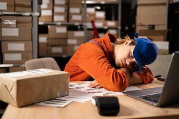Lazy female worker sleeping at the table with boxes in working hours in warehouse. Storage interior.