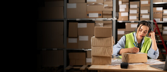 a woman staff in a distribution warehouse in a headset sits at a table takes an order from a...