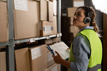 A warehouse worker checks the items against an inventory list on a clipboard. A logistics manager takes inventory using a warehouse management system