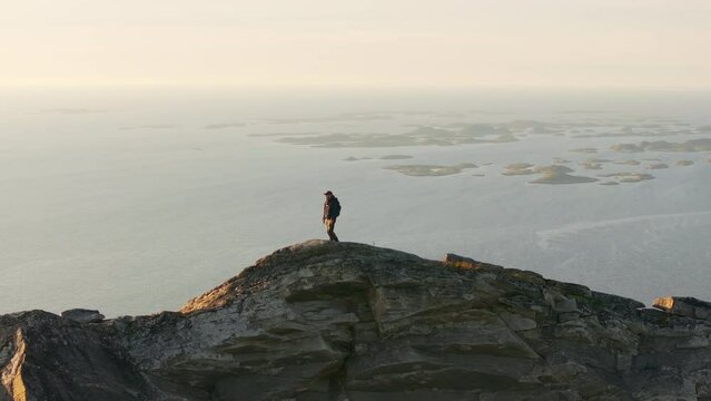 Drone telephoto view of climber on arctic mountain top in midnight sun; drone