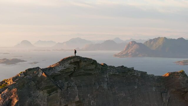 Lone hiker on arctic Norway island mountain ridge top in midnight sun: drone