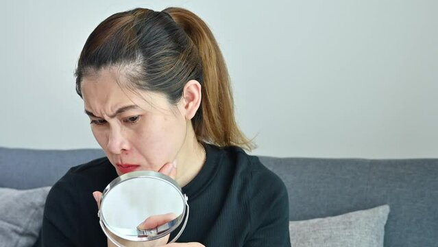 Worried Asian woman having bad emotional about acne inflammation and acne scar occur on her face.