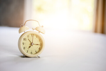 Analog alarm clock on white bed, time in the morning with a bright sunshine