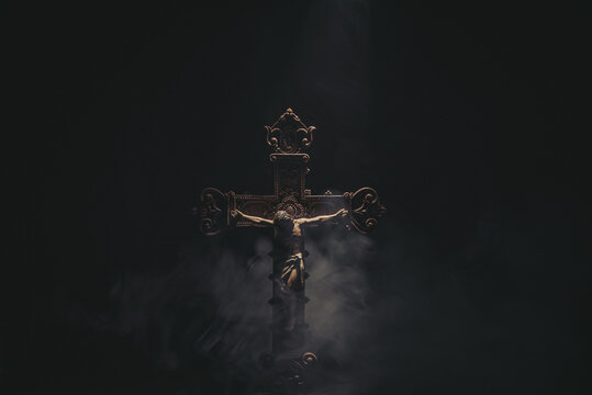 Jesus Christ on a wooden cross with a black background and smoke.
