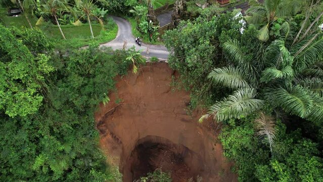 Steep slope has collapsed and damaged edge of road, dangerous landslide that will cause ground to collapse even more under bad circumstances. Aerial view, camera descends down, showing slice of ground