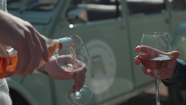 Slow motion shot of hands pouring rose wine into glasses in front of a Deux Chevaux