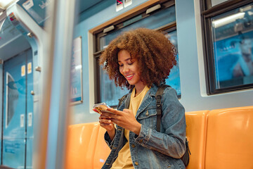Happy young African American woman passenger smile and using smart mobile phone in subway train...