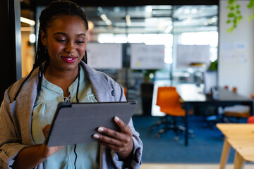 Happy plus size african american casual businesswoman using tablet in office, copy space