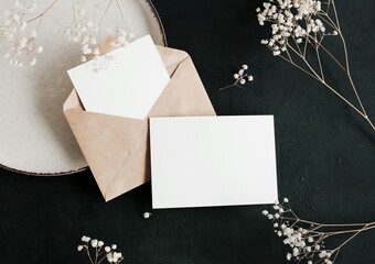 Cards mockup, envelope and dried gypsophila flowers top view on dark green textured background with...