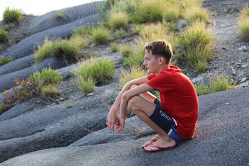 the boy sits against the background of the mountain and looks into the distance