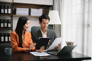 Asian business colleague business presents and explains and using laptop and tablet. Teamwork, financial marketing team,   while sitting in modern office