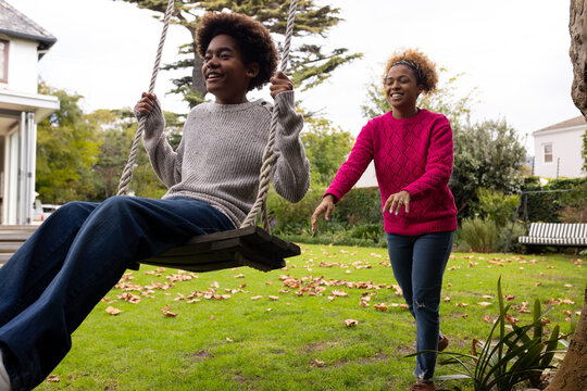 Happy african american mother and son swinging on tree swing in garden
