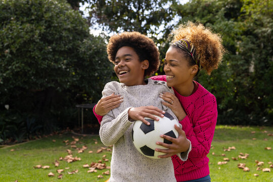 Happy african american mother and son holding ball and embracing in garden