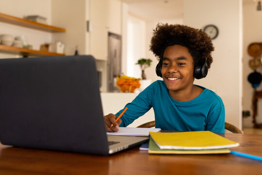 Happy african american boy sitting at table using laptop for online class - Powered by Adobe