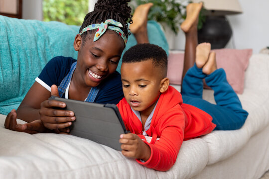 Happy african american brother and sister using tablet on sofa at home