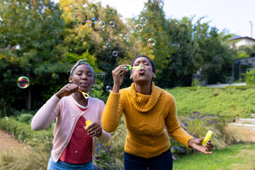 African american mother and daughter blowing bubbles in garden at home