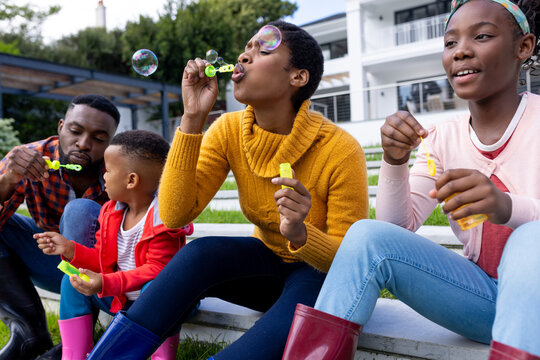 African american couple with son and daughter blowing bubbles in garden at home