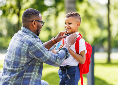 Father escorts happy first-grader boy to school, straightens his bow tie  .