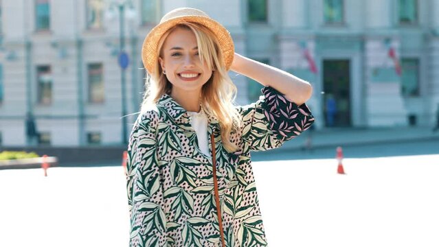 Young beautiful smiling hipster woman in trendy summer clothes. Carefree model posing in the street background at sunset. Positive blond female. Cheerful and happy. In hat 