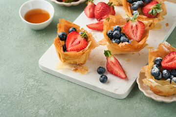 Phyllo or filo pies with fresh berries strawberries and blueberries, cheese filling topped with fresh mint on white plate. Homemade Filo pastry paskets. Delicious filo pastry dessert.