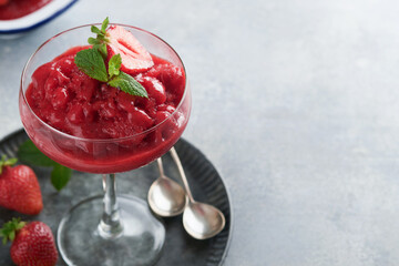 Strawberry granita or fresh berry sorbet in glass on old  grey table background. Texture of ice cream or sorbet. Ice cream with strawberry and mint. Sorbet recipe. Summer treat. Selective focus.