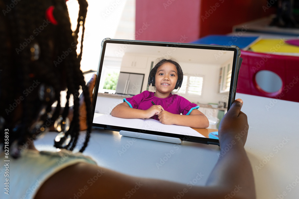 Sticker Rear view of african american girl having a video call on tablet with biracial girl at school