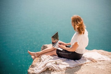 Freelance woman working on a laptop by the sea, typing away on the keyboard while enjoying the beautiful view, highlighting the idea of remote work.