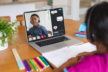 Rear view of biracial girl having a video call with african american boy on laptop at home - Powered by Adobe